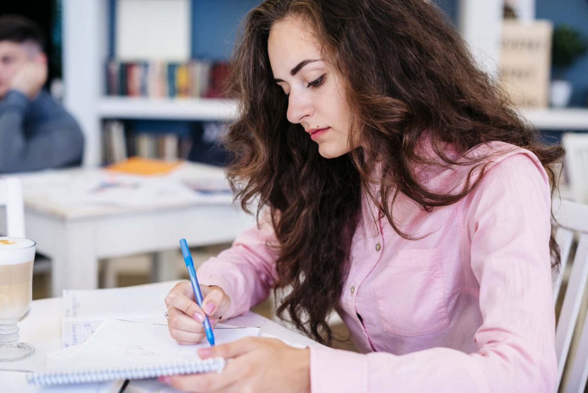 Estudante estuda com caderno e caneta em biblioteca