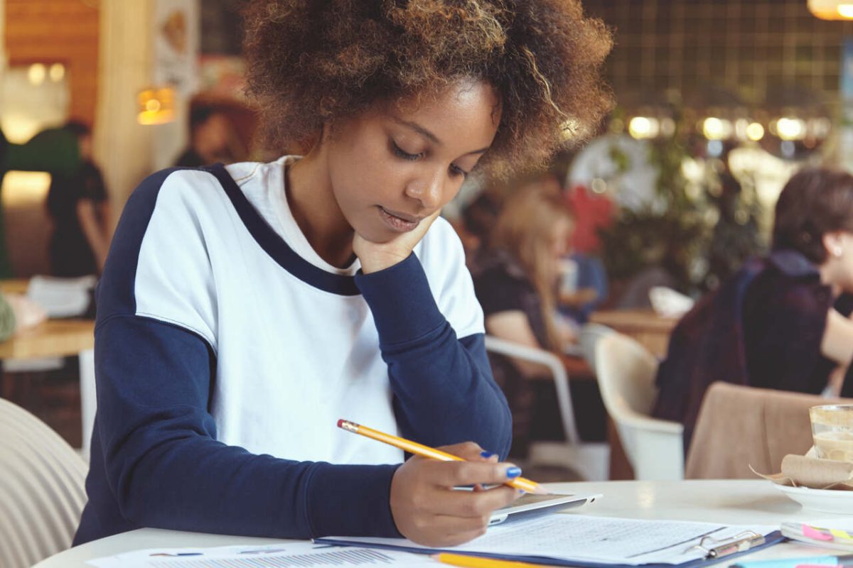 Estudante negra com lápis, tablet e folhas de caderno estudando em biblioteca