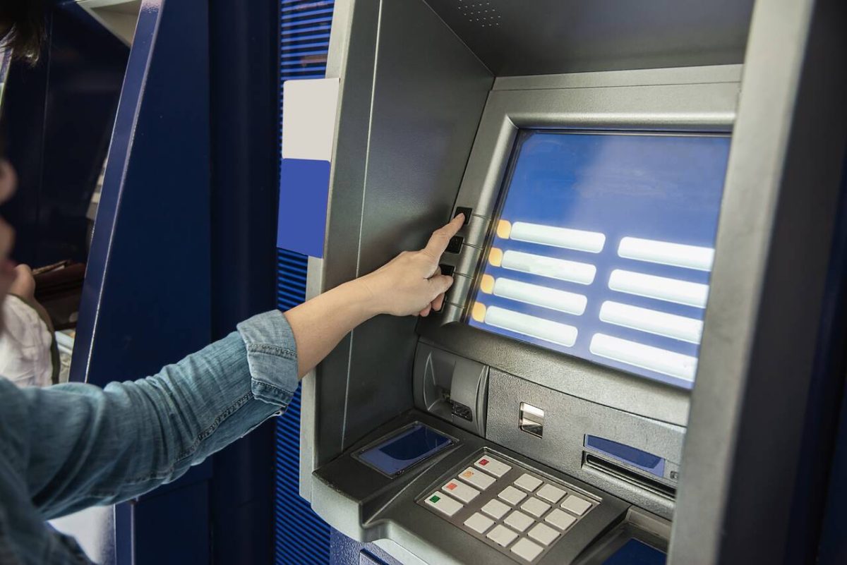 Mulher checa saldo em caixa eletrônico banco