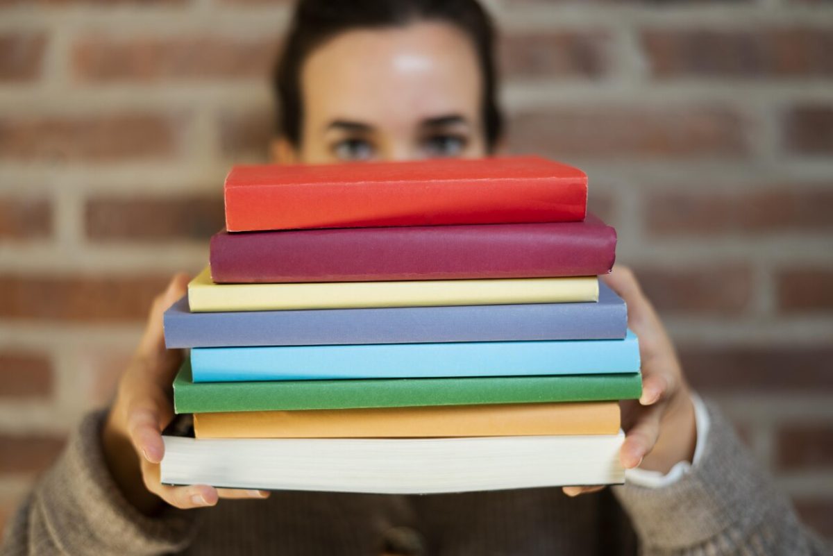 Mulher segura pilha de livros para estudar para concursos administrativos