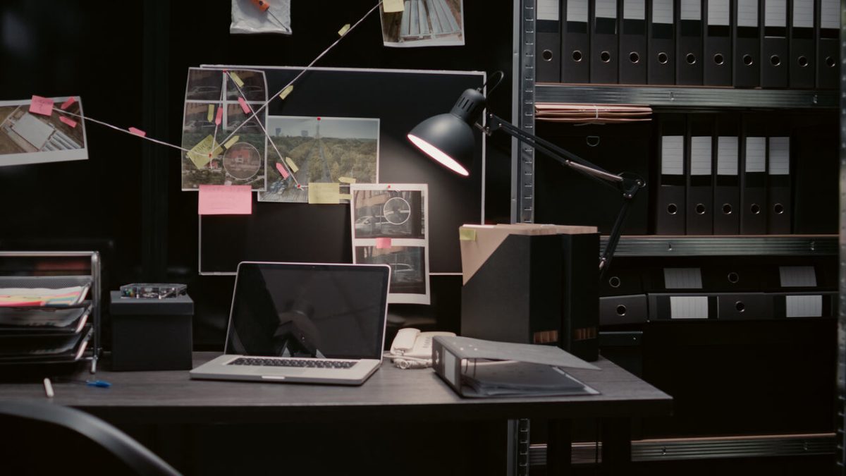 Sala de investigação com notebooks, pastas, luminária, fotos e quadro