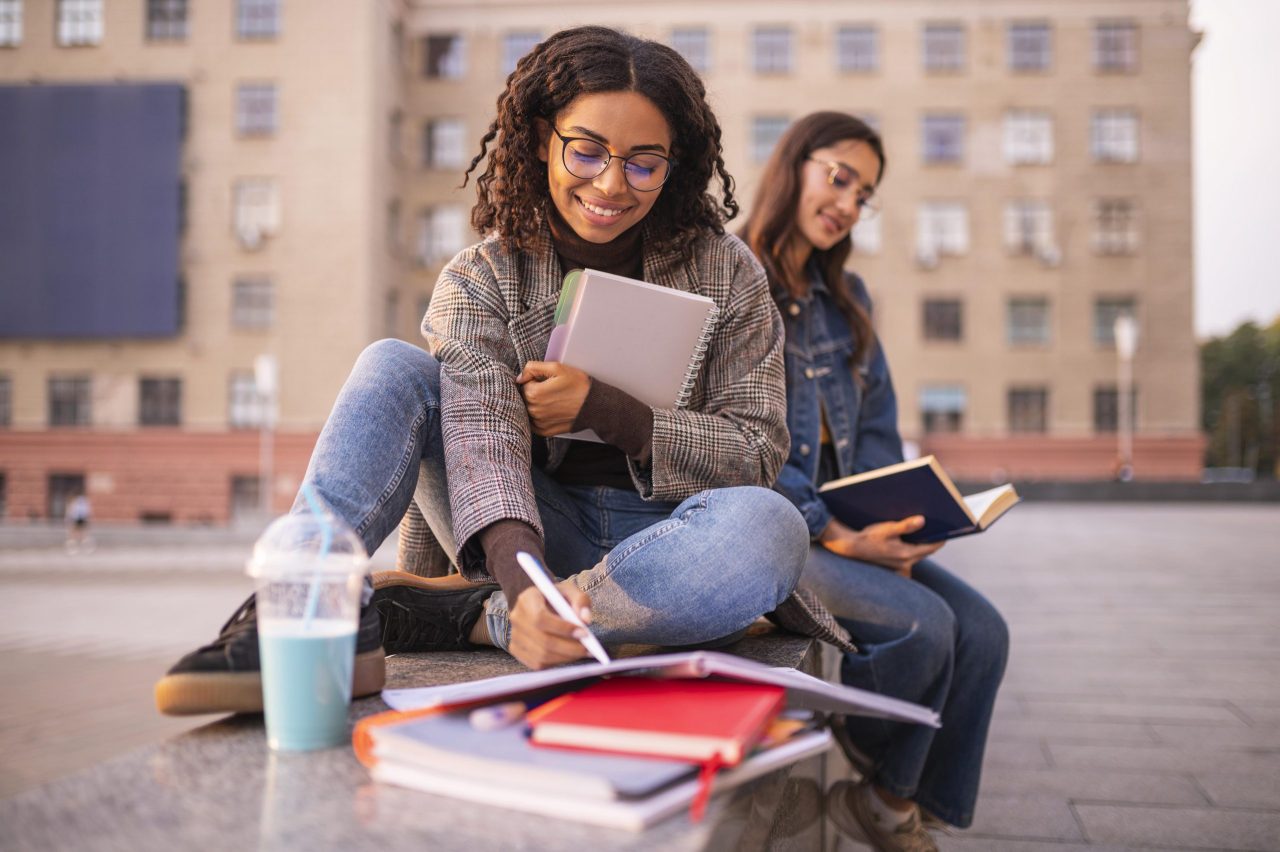 Duas estudantes com livros, cadernos e canetas estudando 