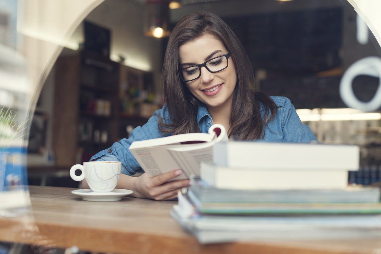 Mulher estudando em biblioteca com livros e xícara de café 