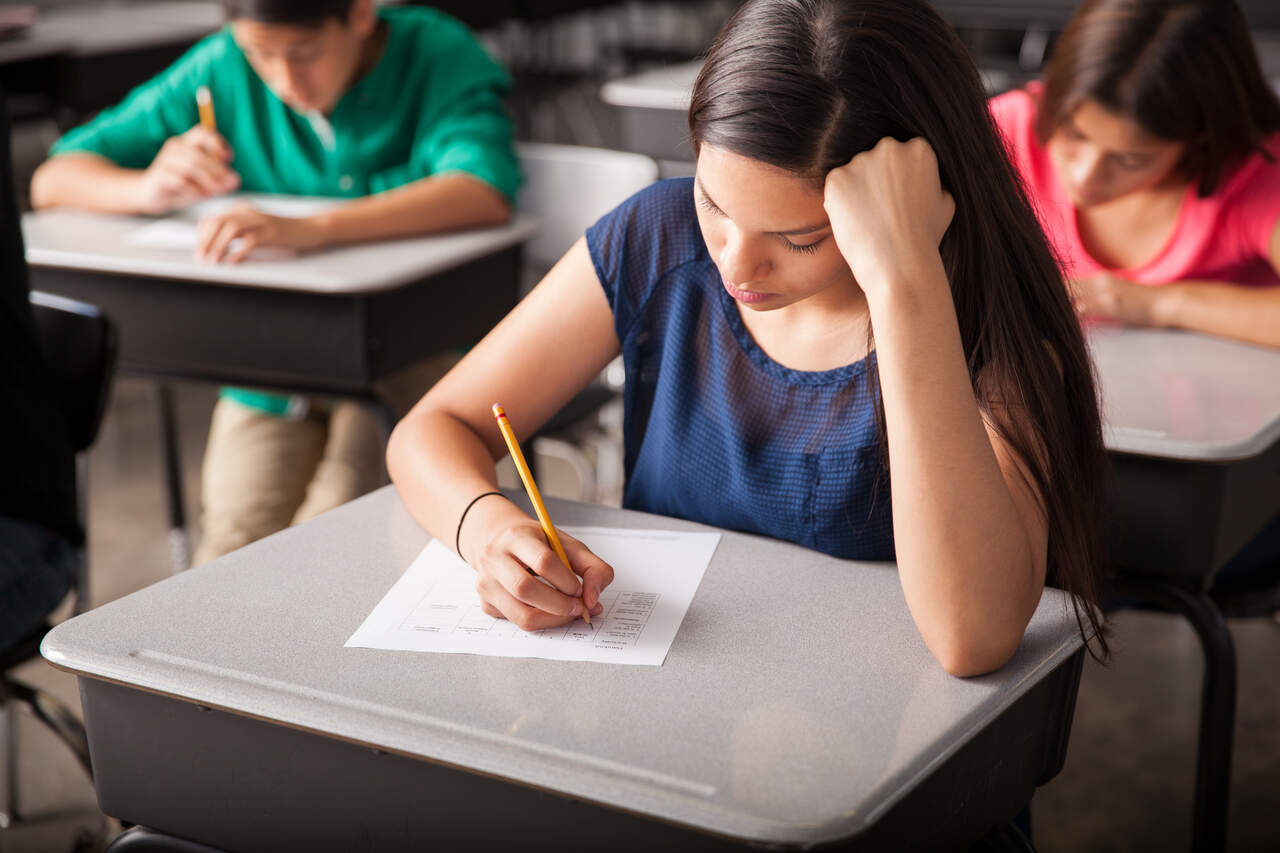 Estudante fazendo prova em mesa com lápis e folha de prova 