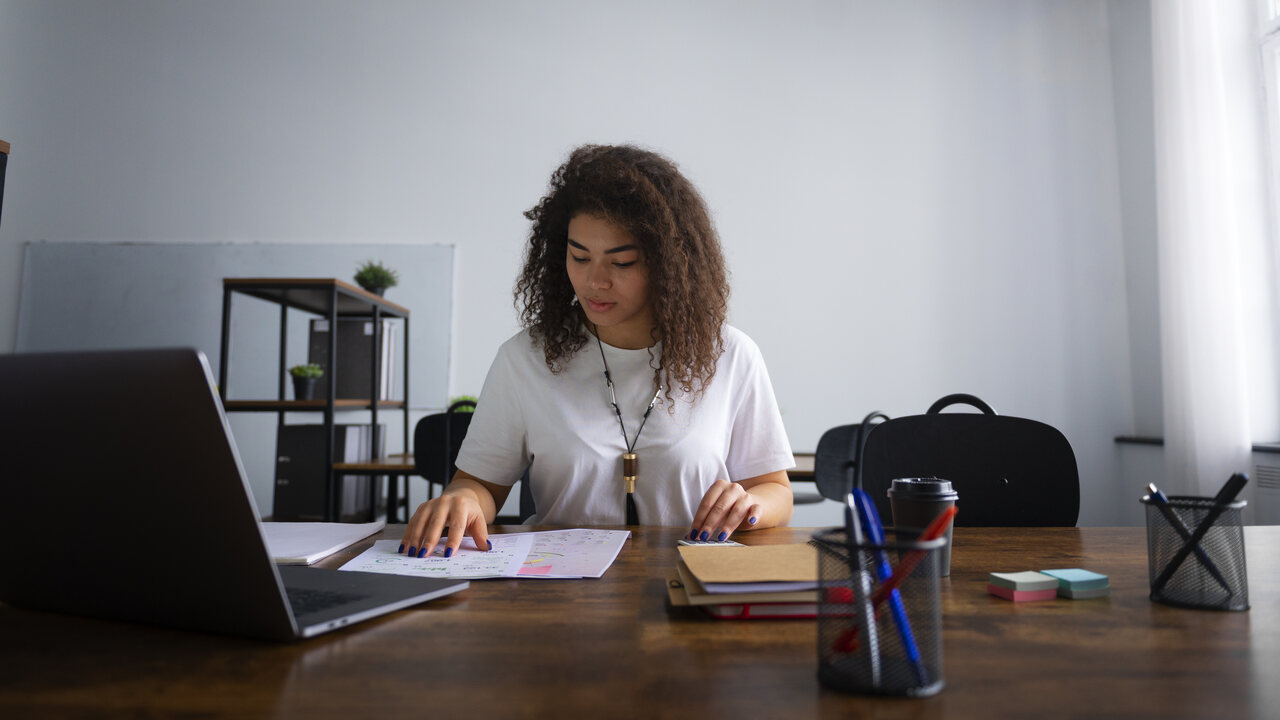 Estudante sentada em mesa de escritório com canetas, notebooks e cadernos 