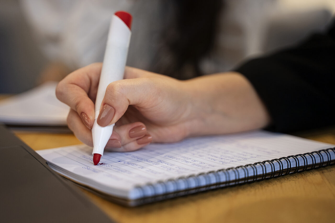Mão feminina com caneta vermelha e caderno 